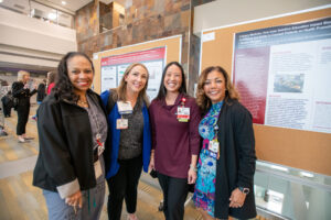 Women pose for photo in front of research poster